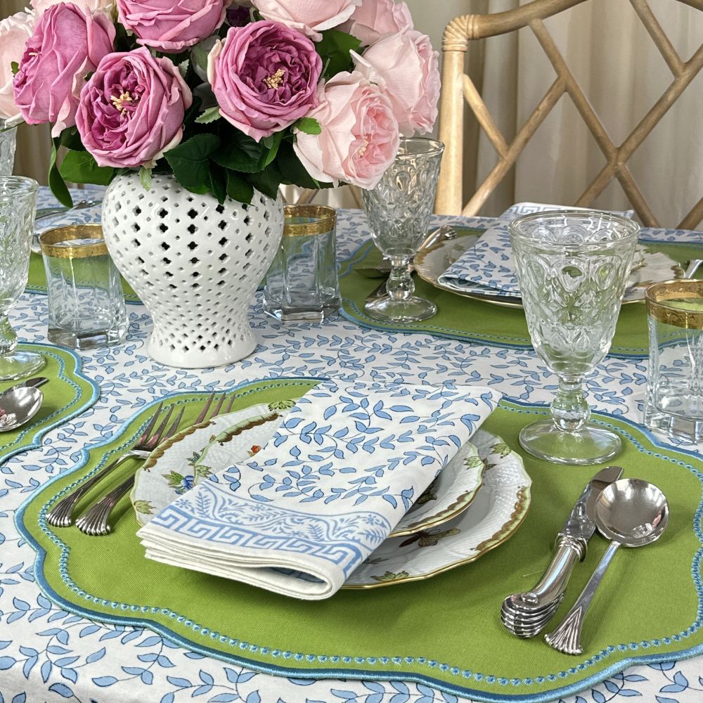 Elegant table setting with floral centerpiece, green placemats, and patterned plates. Blue leaves block print napkin . 