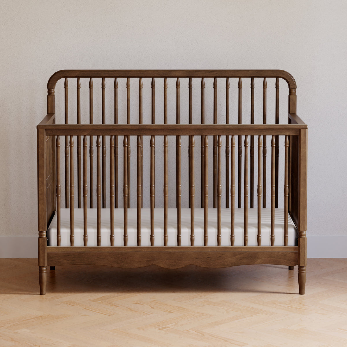 Front view of Liberty 4-in-1 convertible spindle crib showcasing turned spindles and walnut finish against a neutral wall