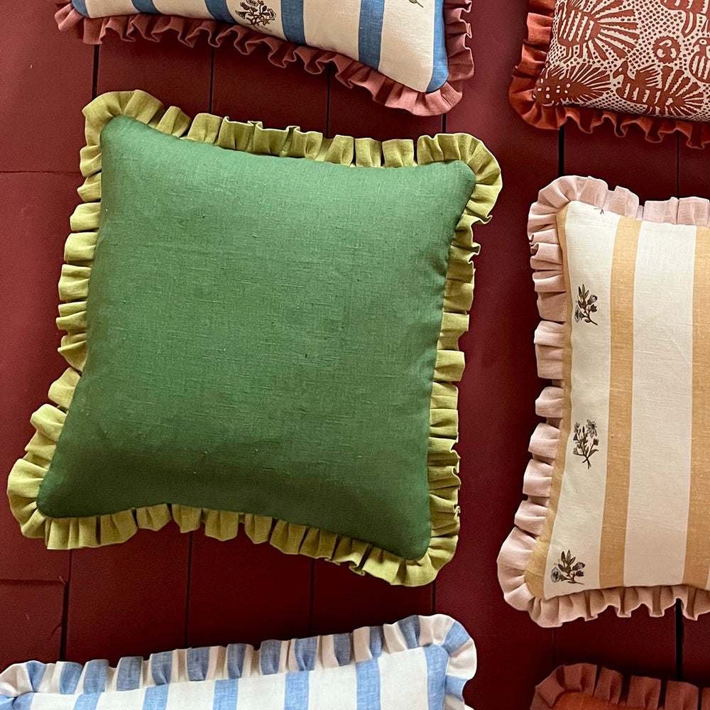 Front view of Constantia Green cushion showcasing its green plain weave and Moss Green frill against a burgundy backdrop