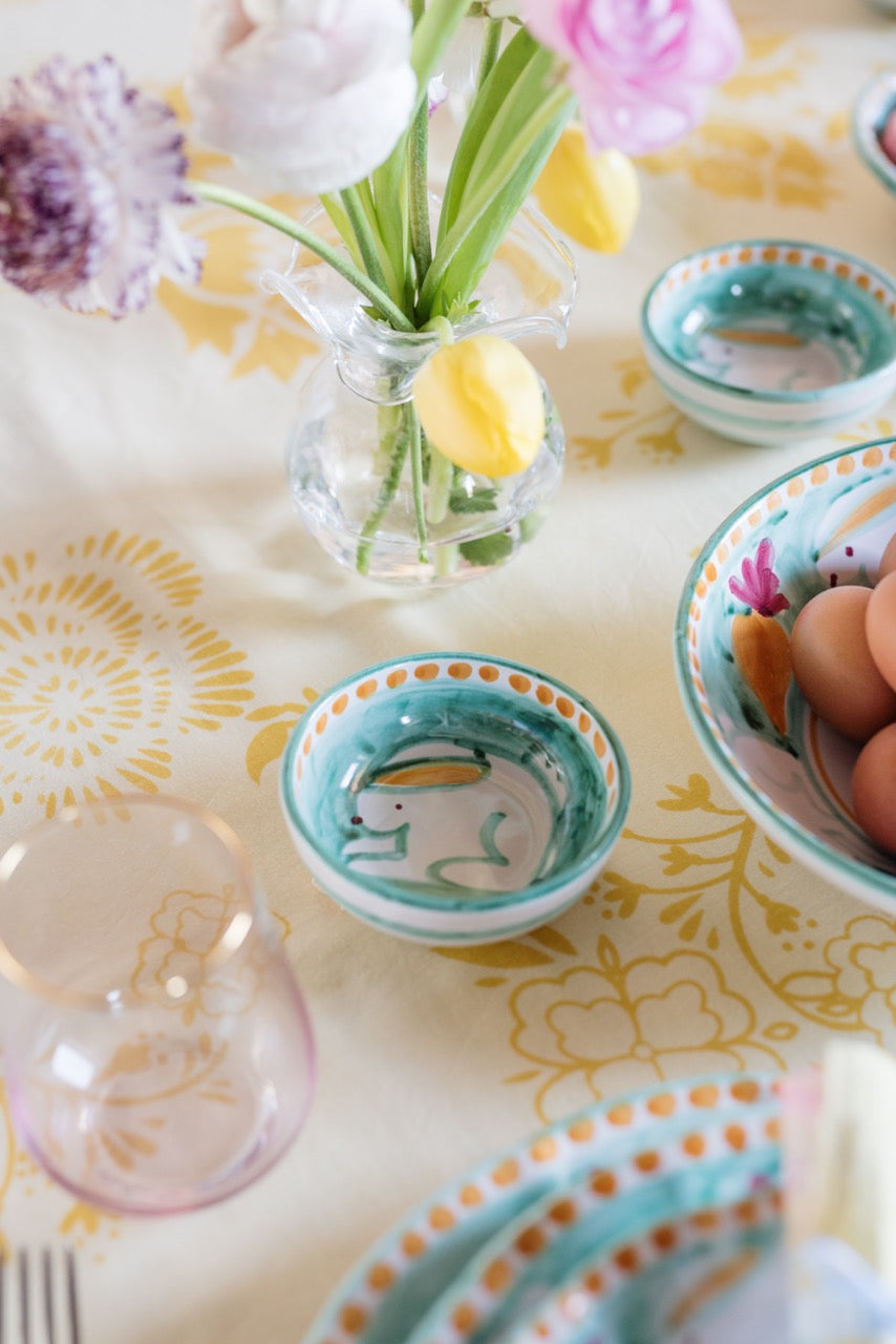 Campagna olive oil bowl on a sunlit patterned tablecloth beside a vase of tulips and matching ceramic bowls