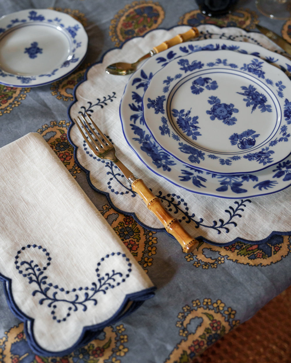 Overhead view of Gloria porcelain dessert plate in blue showing blue floral pattern on white with linen and bamboo fork