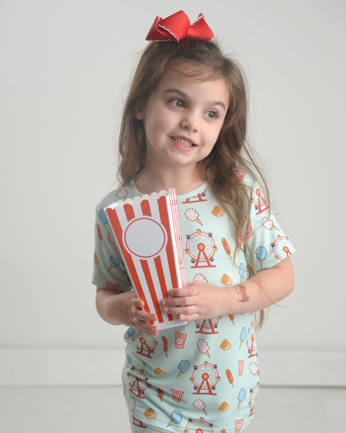 Front view of Carnival bamboo two piece pajama set on child model showcasing light blue carnival print short sleeve top and matching pants with neutral studio background