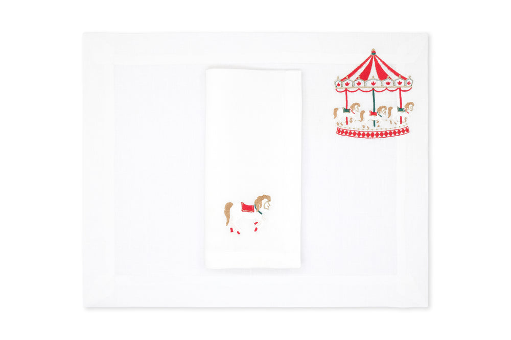 Top view of placemat and napkin set showcasing embroidered red-and-gold carousel motif on white Italian linen background