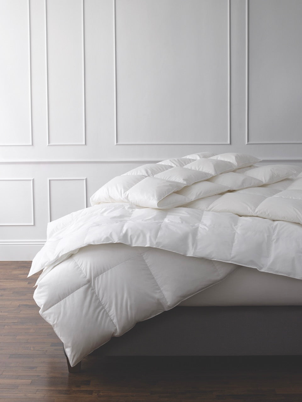 Angled view of Chalet down comforter showing box stitching and lofty fill on a gray platform bed against a white paneled wall