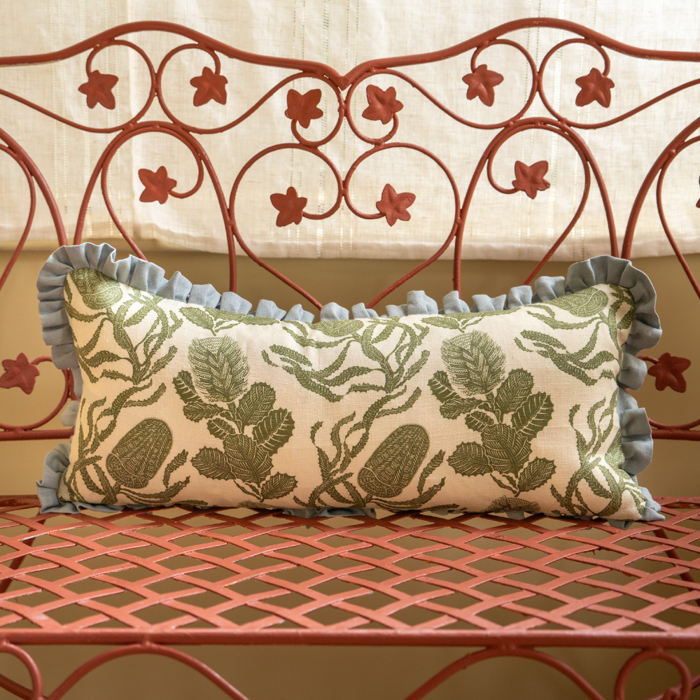 Front view of Cape Botanical Print Cushion showcasing botanical green linen print and Parma Grey frill on a coral metal bench