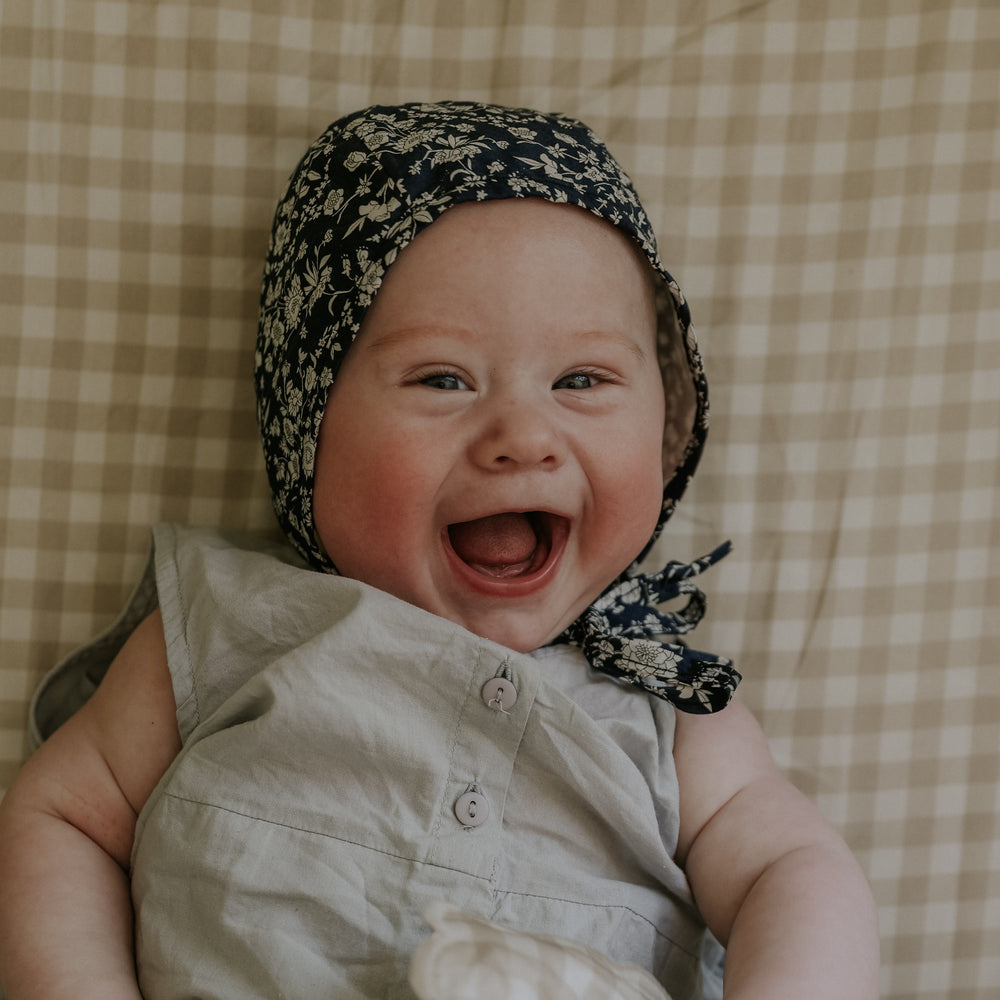 Baby Laying on top of Crib Sheet in the Beige color of the Picnic Gingham Print