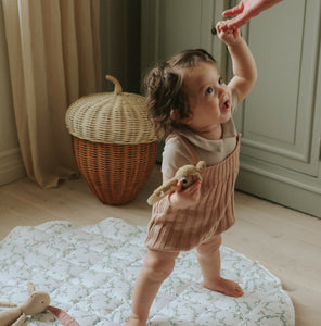 Secret Garden play mat in Ivory. Child is standing up on play mat holding grown ups hand, while holding a rattle in her other hand. 