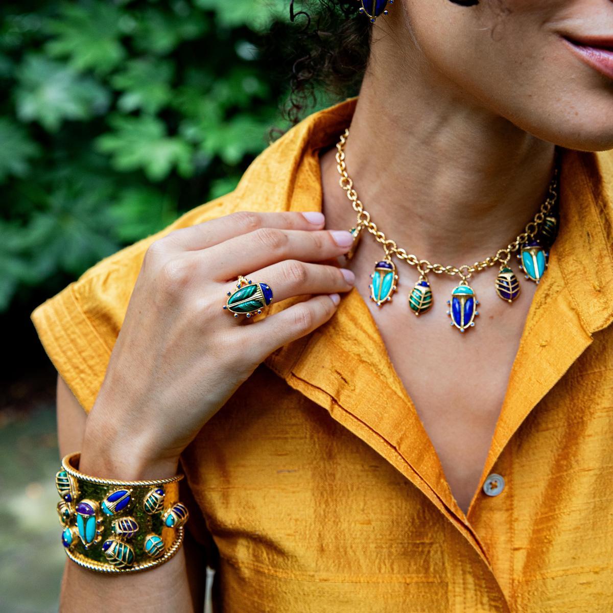 Model wearing Scarab Grande ring with lapis and malachite, matching scarab necklace and cuff on a mustard shirt