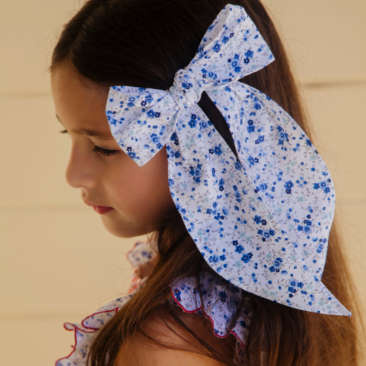 Close-up side view of Emmie Bow floral hair bow showcasing blue floral print and long ribbon tails on a girl’s dark hair