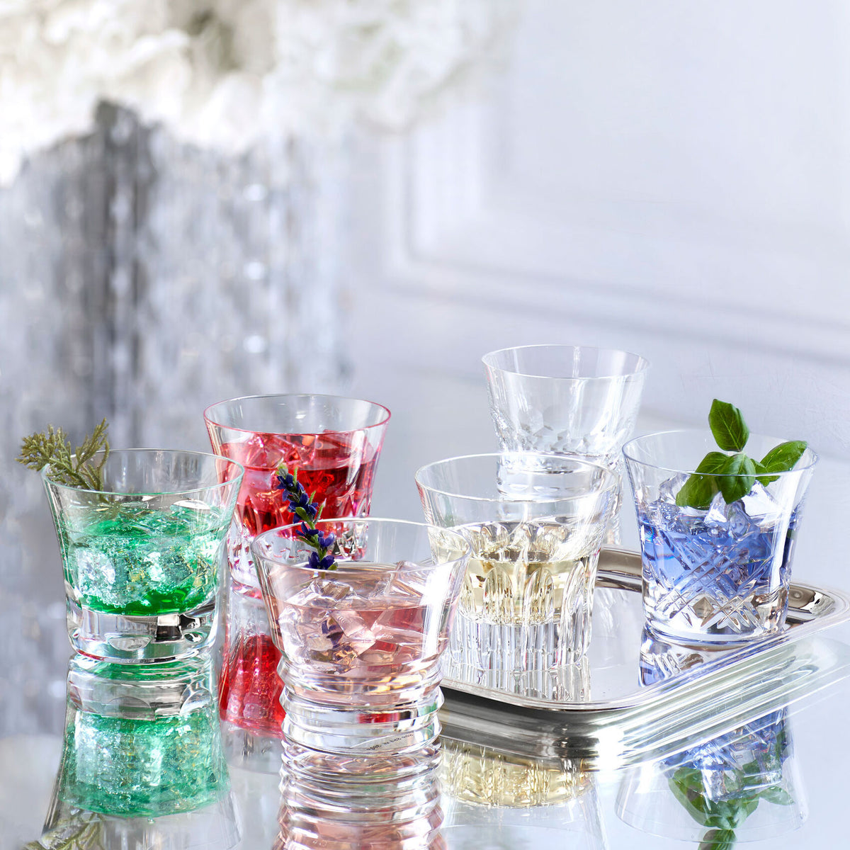 Six Baccarat crystal highball glasses with colorful drinks and garnishes on a mirrored tray