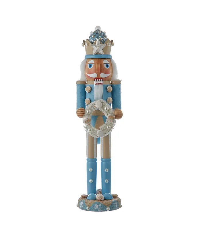 Front view of 15-inch wooden beach nutcracker with blue-and-beige paint, glittered sand hat, pearl accents, and shell wreath on white background
