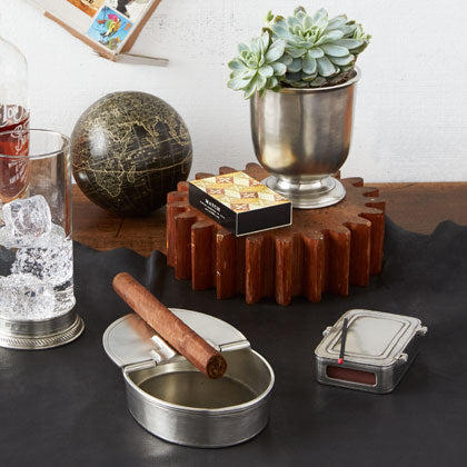 Three-quarter view of pewter lidded match box with wood matches and striker on leather tabletop