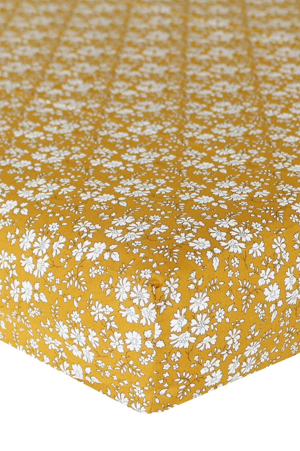 Angled close-up of Fitted Sheet Made With Liberty Fabric in Capel Mustard showcasing its white floral pattern on a white background