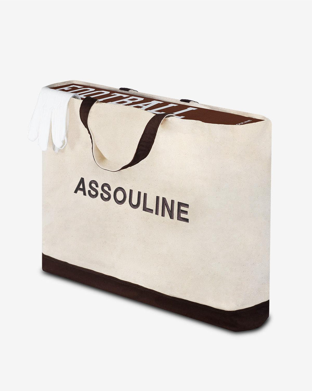 American Football: The Impossible Collection by Assouline: three-quarter view of the canvas carry bag included with the edition; the landscape-format natural cream canvas bag has ASSOULINE in large dark charcoal block letters on the face and a dark espresso base panel; dark brown fabric handles; the top of the brown pebbled-leather box sticks out from the bag with FOOTBALL in white type on the spine; white tissue paper at the top; white background