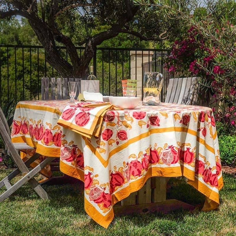 Displayed French Tablecloth Pomegranate with ruby red and citrine yellow pomegranate pattern on an outdoor dining table