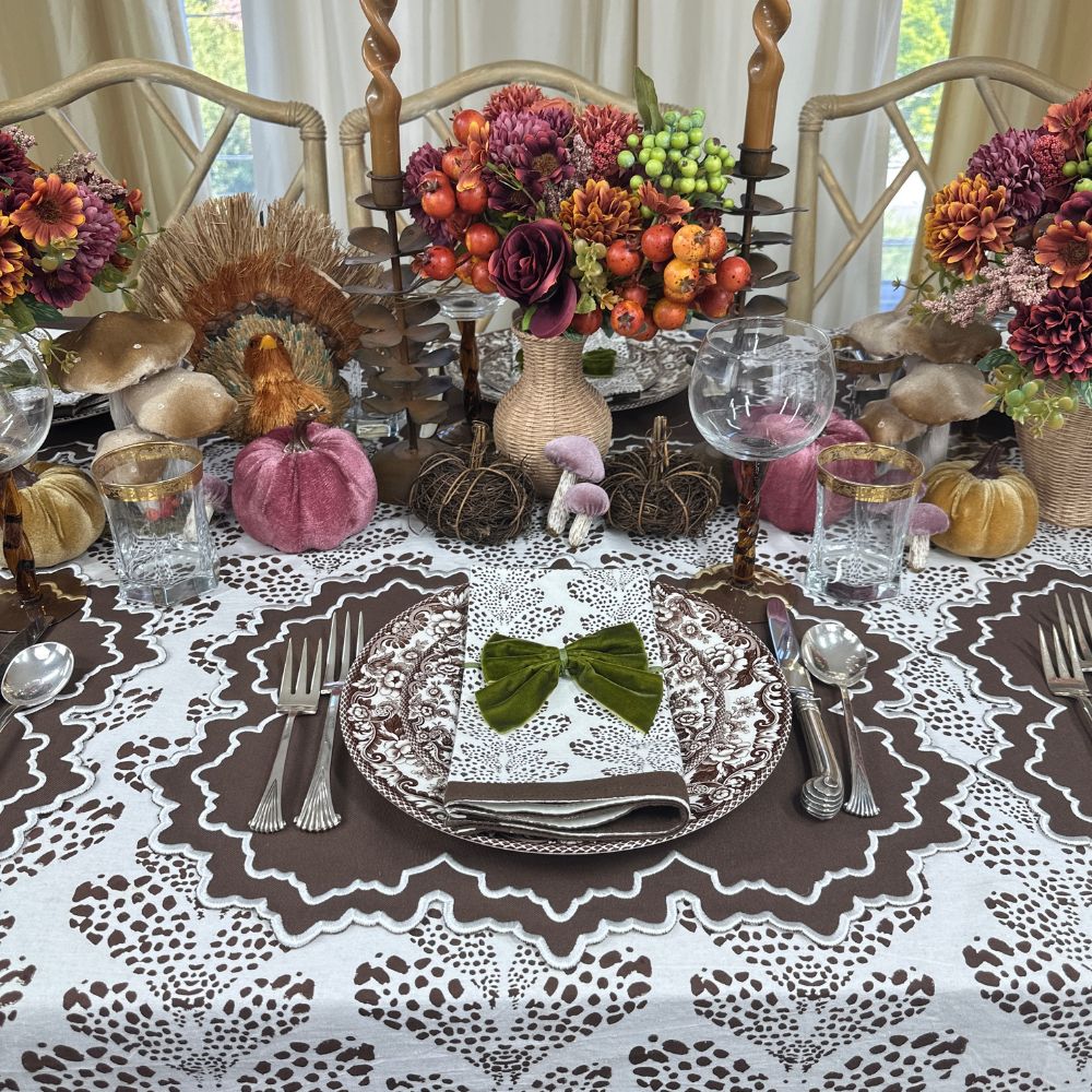 Decorative table setting with pumpkins, flowers, and cutlery on a patterned tablecloth. Luxury embroidered placemat and block print napkin