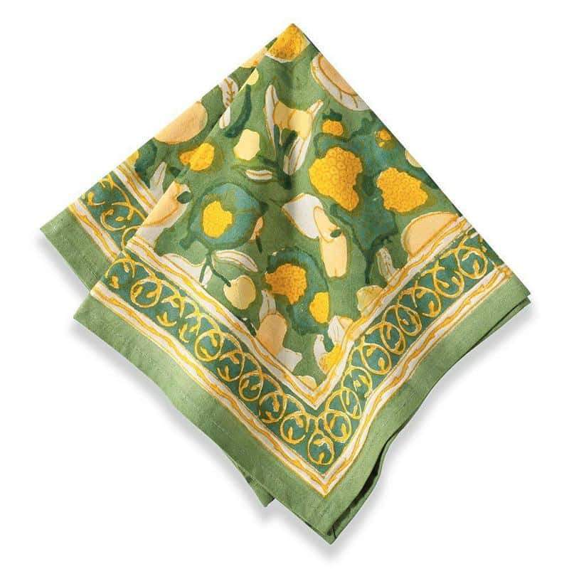 Top-down view of a folded yellow and green fruit-patterned linen napkin showcasing hand-painted fruit print and decorative border on white background