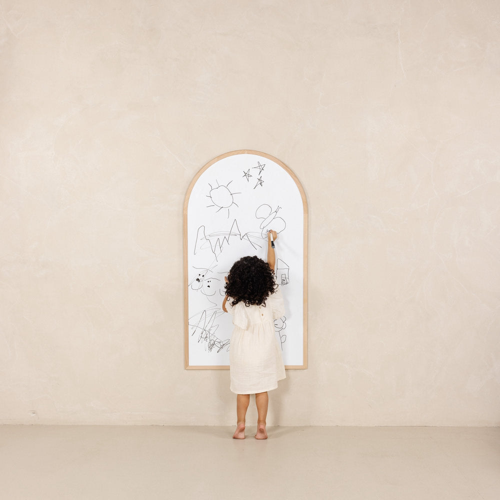 Child drawing on the whiteboard side of the Play Chalkboard with beech wood arched frame against a neutral wall