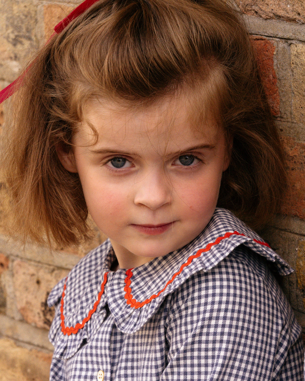 Young girl with a checkered dress against a brick wall