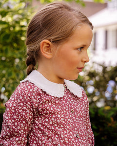 Young girl wearing a red floral dress with a white collar outdoors.