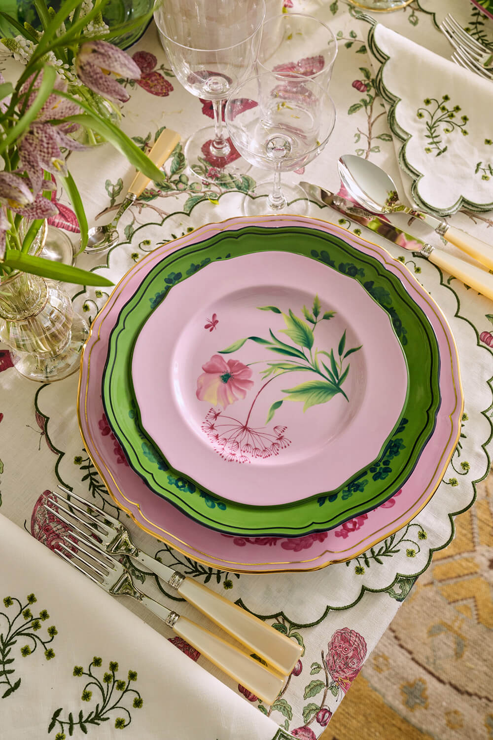 Decorative table setting with floral plates and cutlery on a patterned tablecloth.