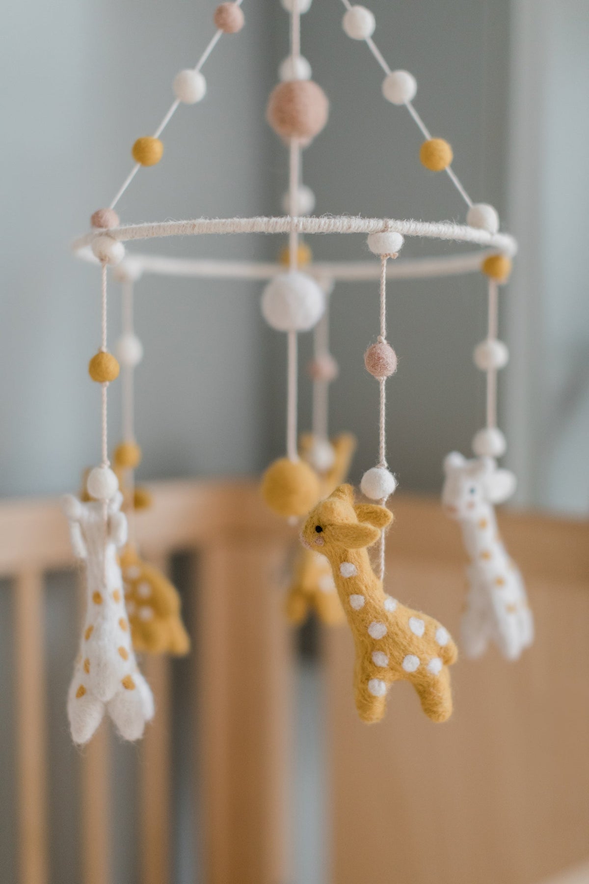 Close up view of Classic Mobile in Gentle Giraffe showcasing felt giraffes and pom pom strands with a nursery background