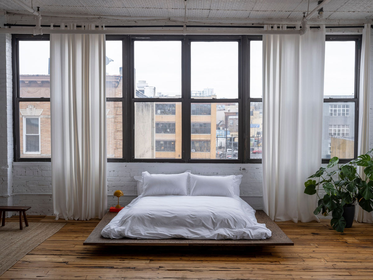 Front view of Relaxed Percale Sheet Set in white on low platform bed showing crinkled percale with loft window background