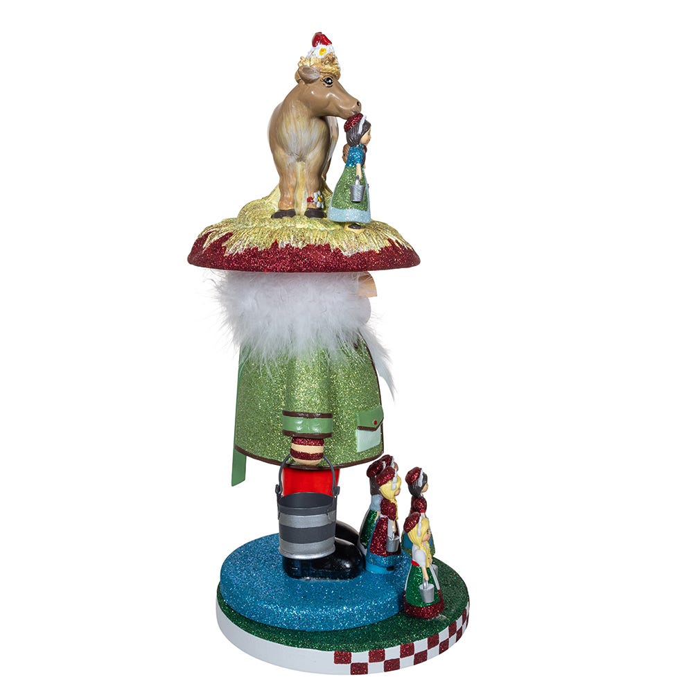 Angled rear view of Eight Maids A Milking nutcracker with green glitter coat, figurines on hat and glittered round base