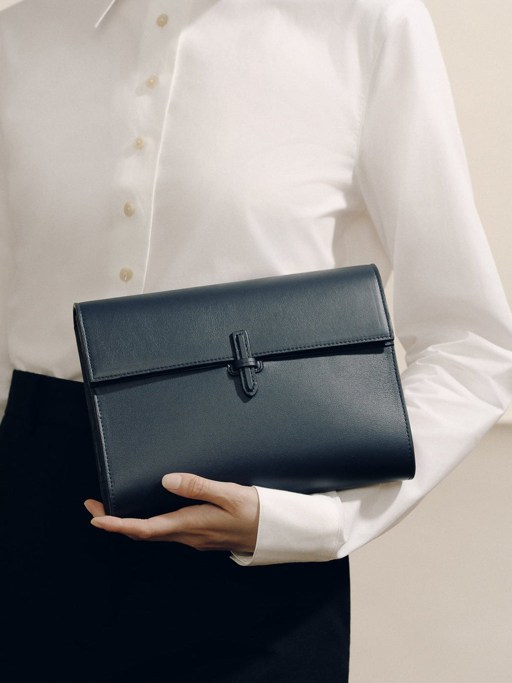 Front view of The Large Soft Clutch in navy nappa showcasing its signature closure while held by a model in a white blouse