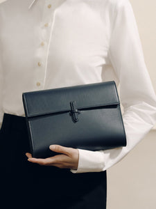 Front view of The Large Soft Clutch in navy nappa showcasing its signature closure while held by a model in a white blouse