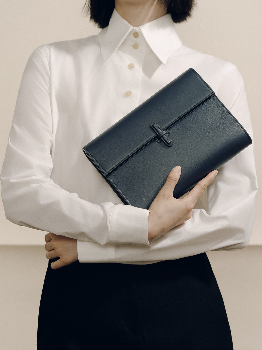 Angled view of The Large Soft Clutch in Navy Nappa showcasing its signature closure with a model in a white shirt
