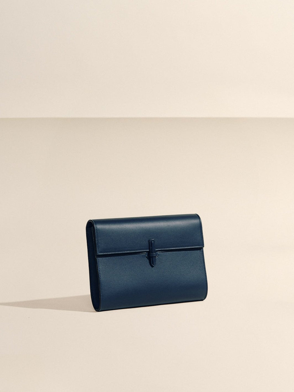 Front view of The Large Soft Clutch in Navy Nappa showcasing its signature closure against a neutral beige background