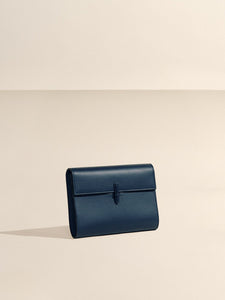 Front view of The Large Soft Clutch in Navy Nappa showcasing its signature closure against a neutral beige background