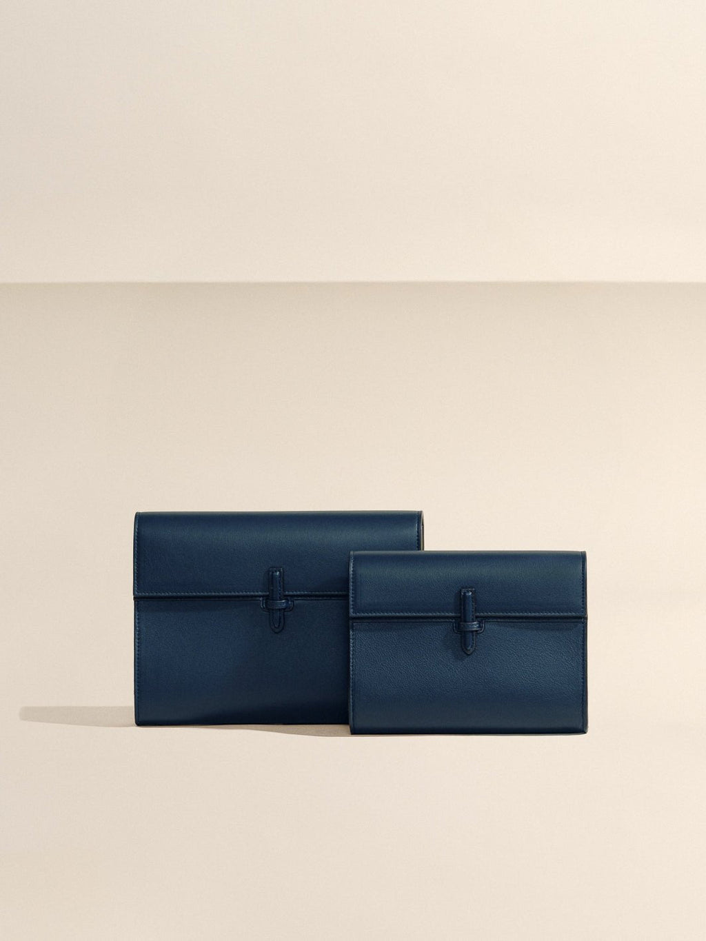 Front view of The Large Soft Clutch in navy nappa leather showcasing its signature closure against a beige background