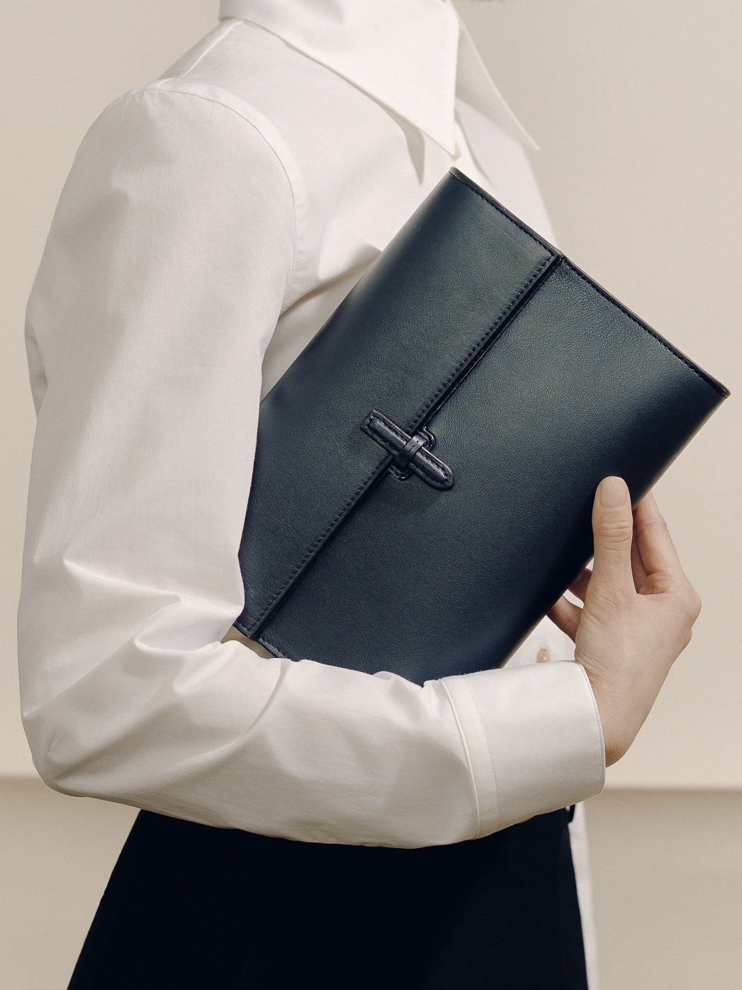 Front view of The Large Soft Clutch in navy nappa leather showcasing its signature closure while held against a model’s white blouse
