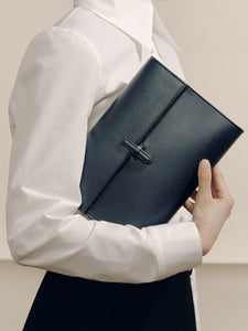 Front view of The Large Soft Clutch in navy nappa leather showcasing its signature closure while held against a model’s white blouse