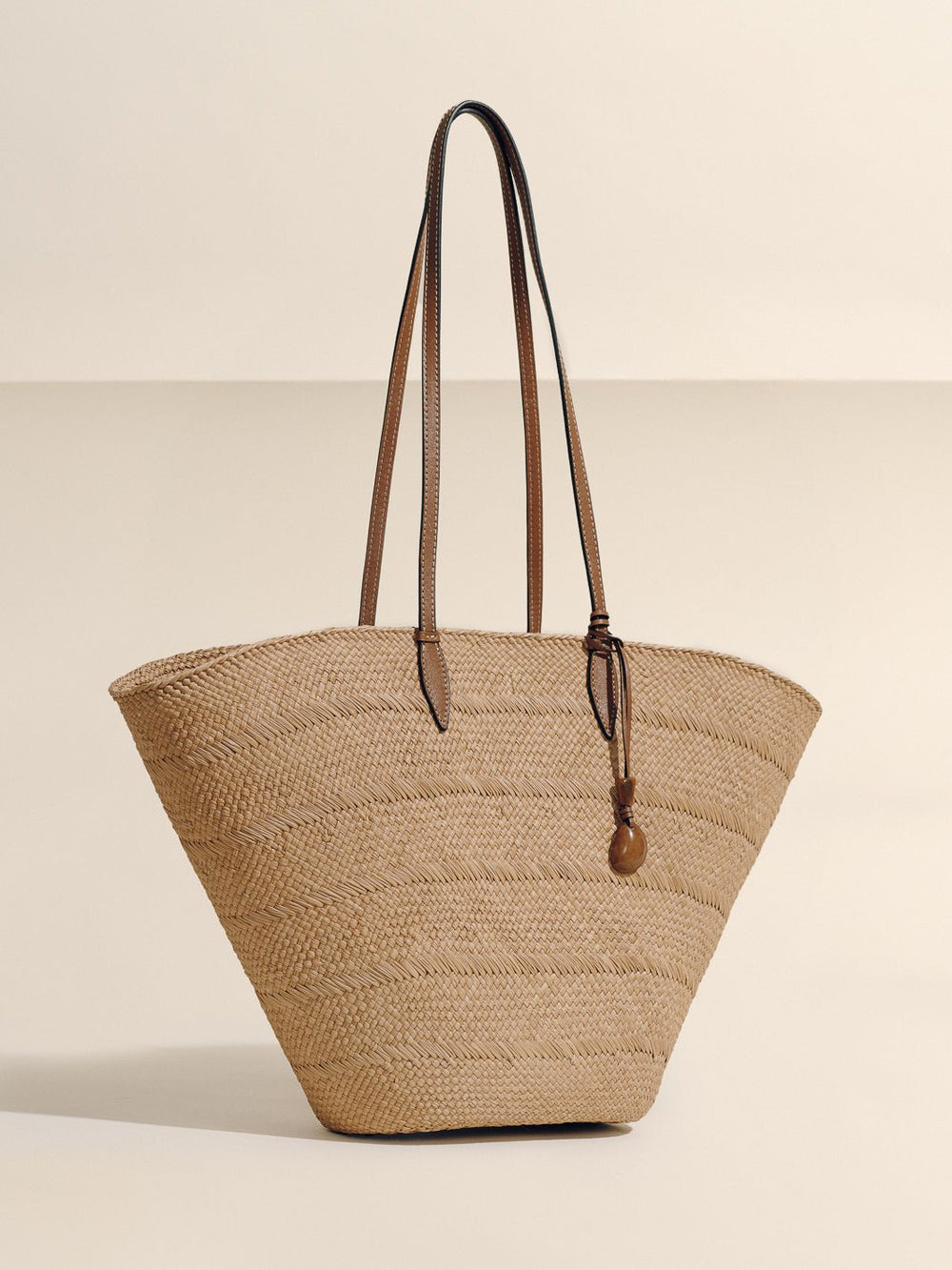 Front view of Large Trapeze Basket in Nuez Cognac showing handwoven iraca body, cognac leather straps, and tagua charm