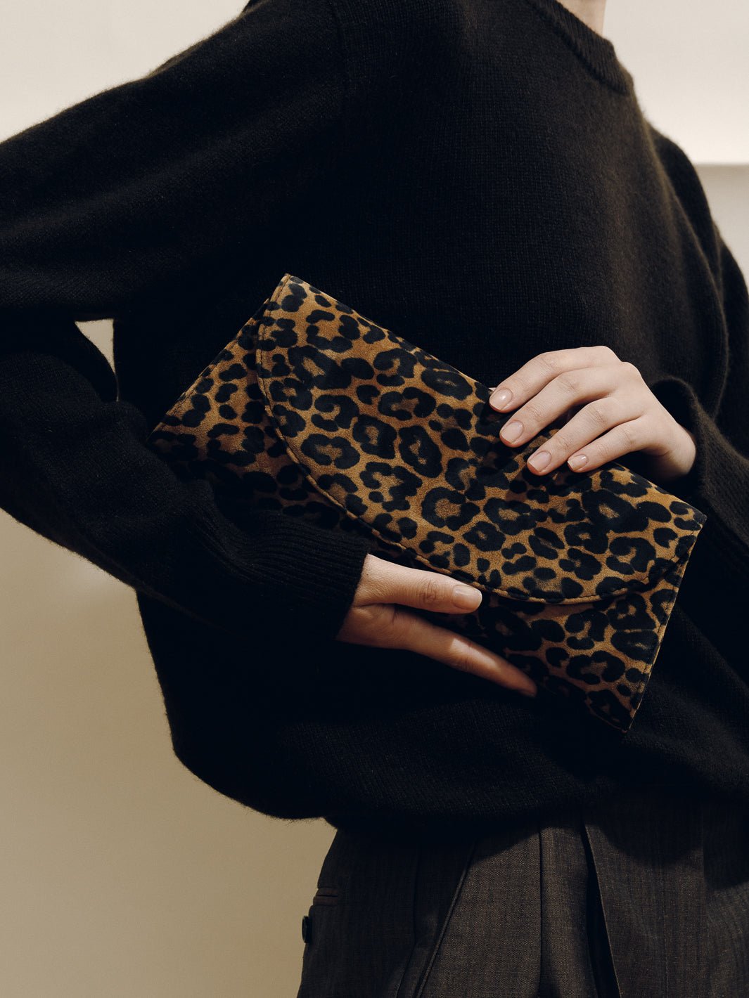 Front view of The Opera Clutch in Leopard Suede showcasing leopard suede and a minimalist silhouette against black clothing