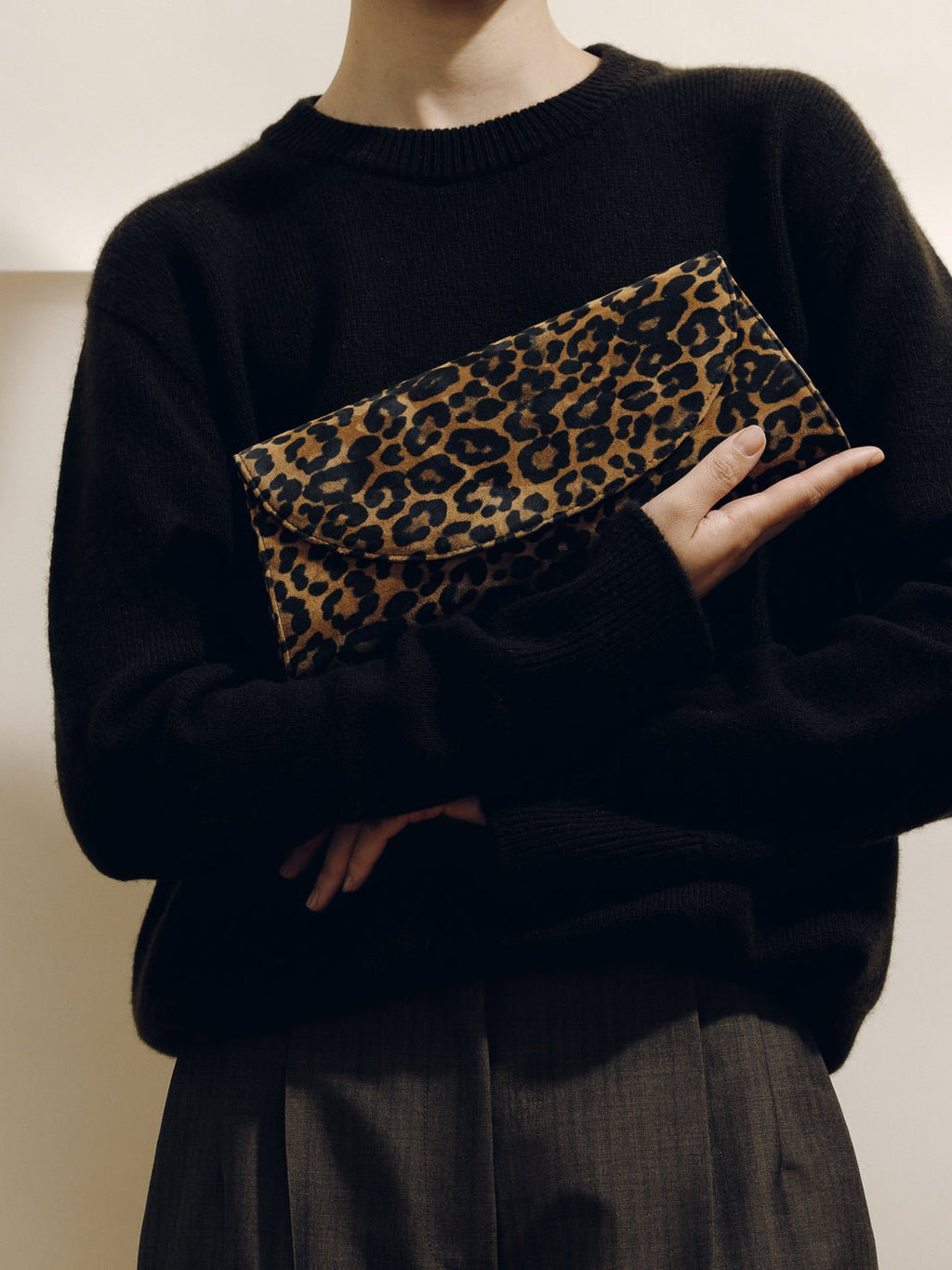 Front view of The Opera Clutch in Leopard Suede showcasing its leopard pattern and slim silhouette with a person wearing black clothing