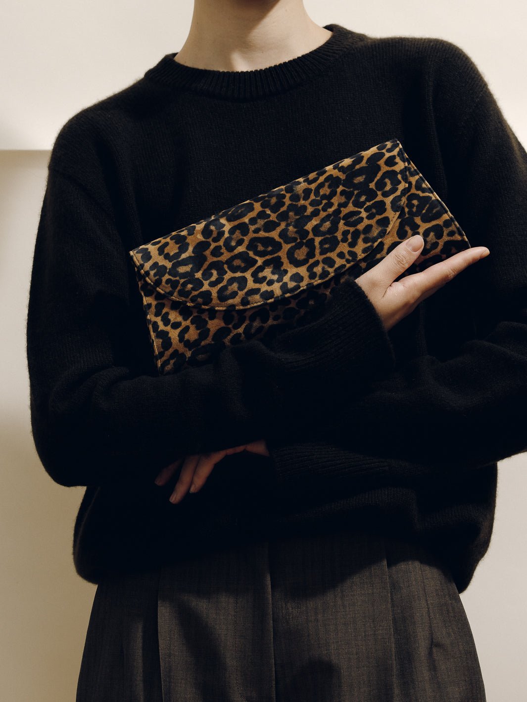 Front view of The Opera Clutch in Leopard Suede showcasing its leopard pattern and slim silhouette with a person wearing black clothing