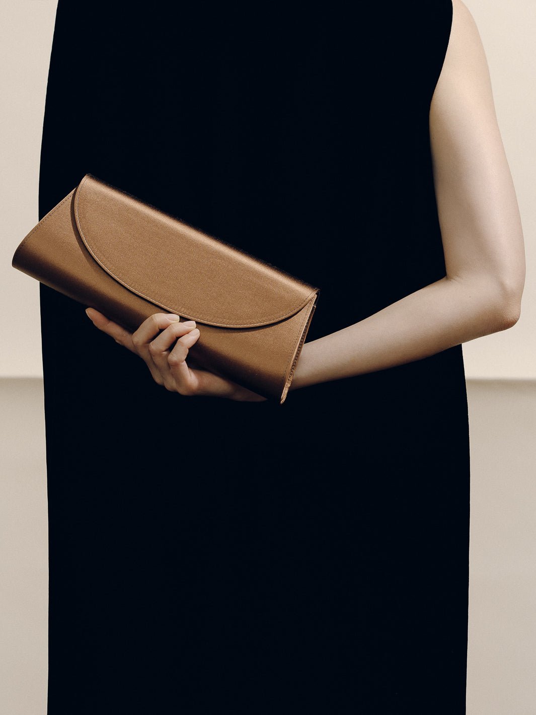 Front view of The Opera Clutch in Dark Brown Satin showcasing its minimalist silhouette with a model in a black dress