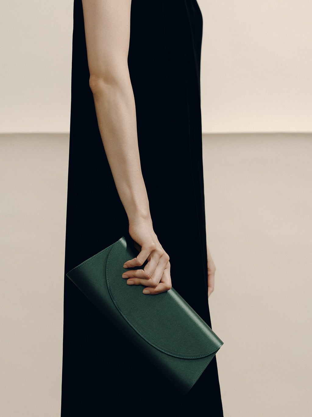 Angled view of The Opera Clutch in Emerald Satin showcasing its minimalist silhouette with a model in a black dress