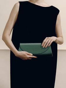 Front view of The Opera Clutch in Emerald Satin showcasing its minimalist silhouette with a model in a black dress