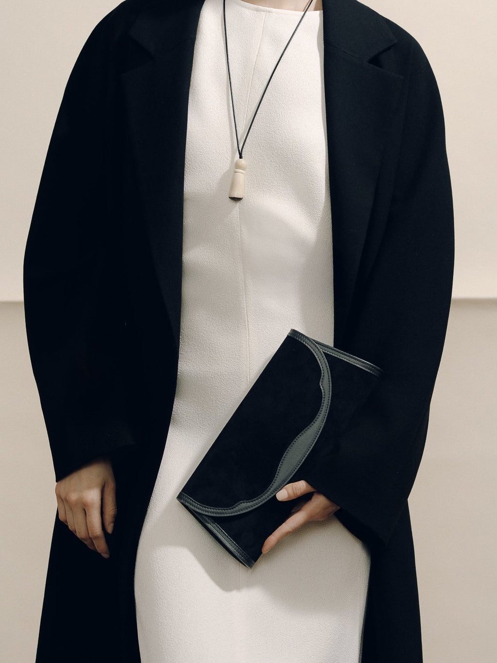Front view of The Opera Clutch in black suede with sculpted Nappa leather Western trim, held by a model in black blazer