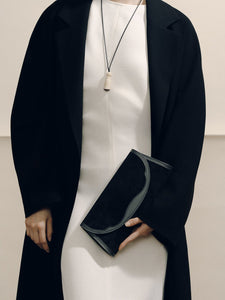 Front view of The Opera Clutch in black suede with sculpted Nappa leather Western trim, held by a model in black blazer