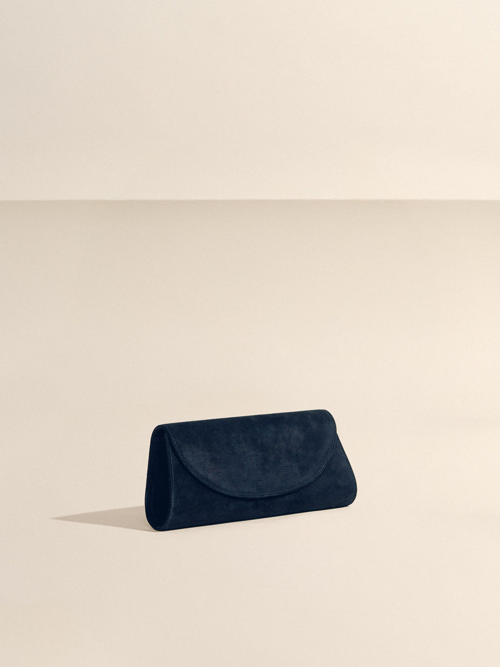 Angled front view of The Opera Clutch in black suede showcasing sculpted Nappa leather Western trim on a beige background