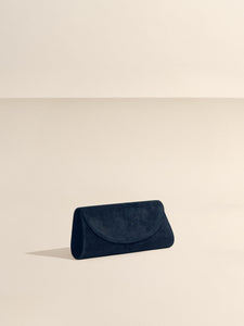 Angled front view of The Opera Clutch in black suede showcasing sculpted Nappa leather Western trim on a beige background