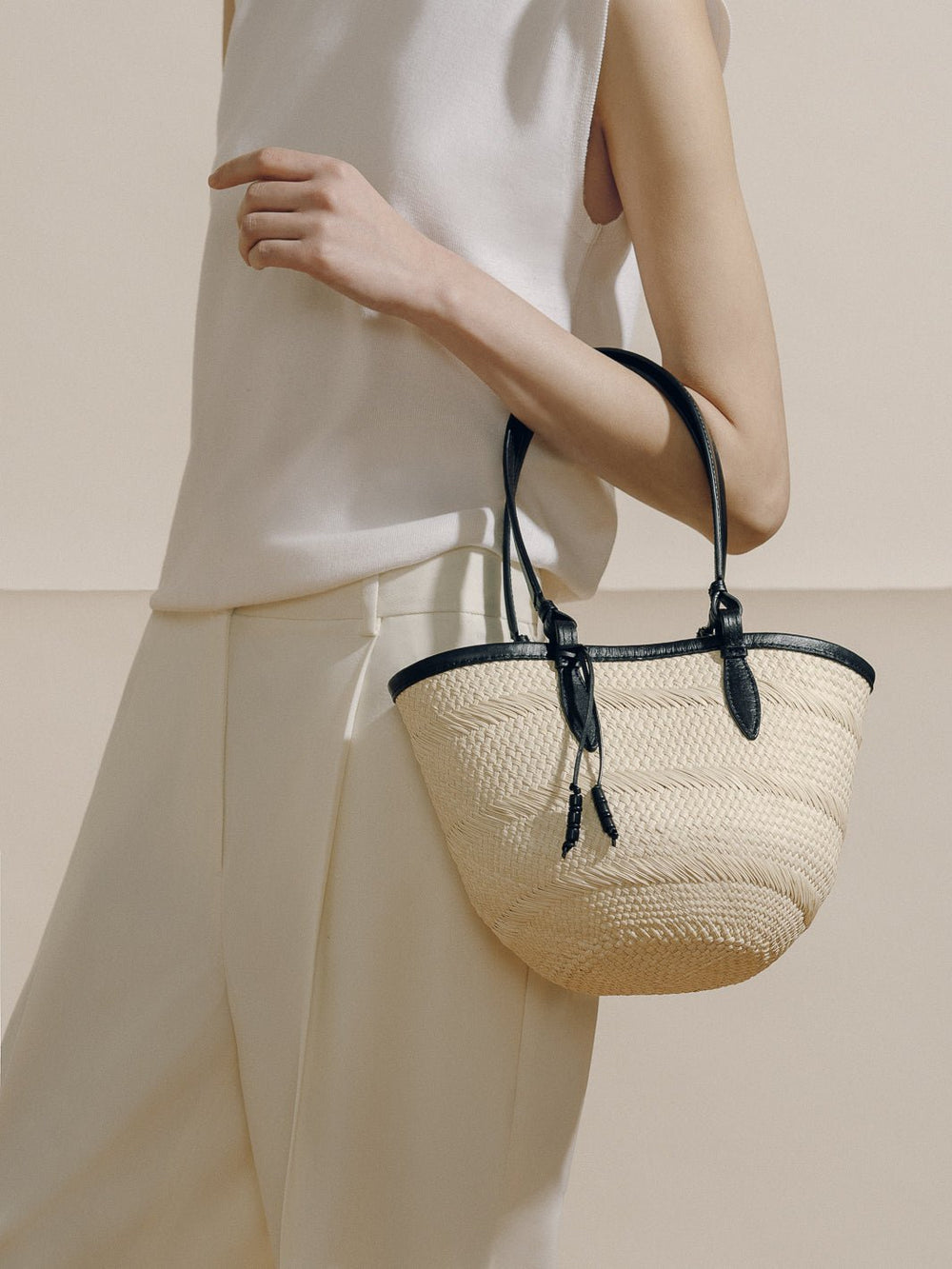 Side view of The Small Basket held by model showing woven iraca straw body with black leather trim and handles