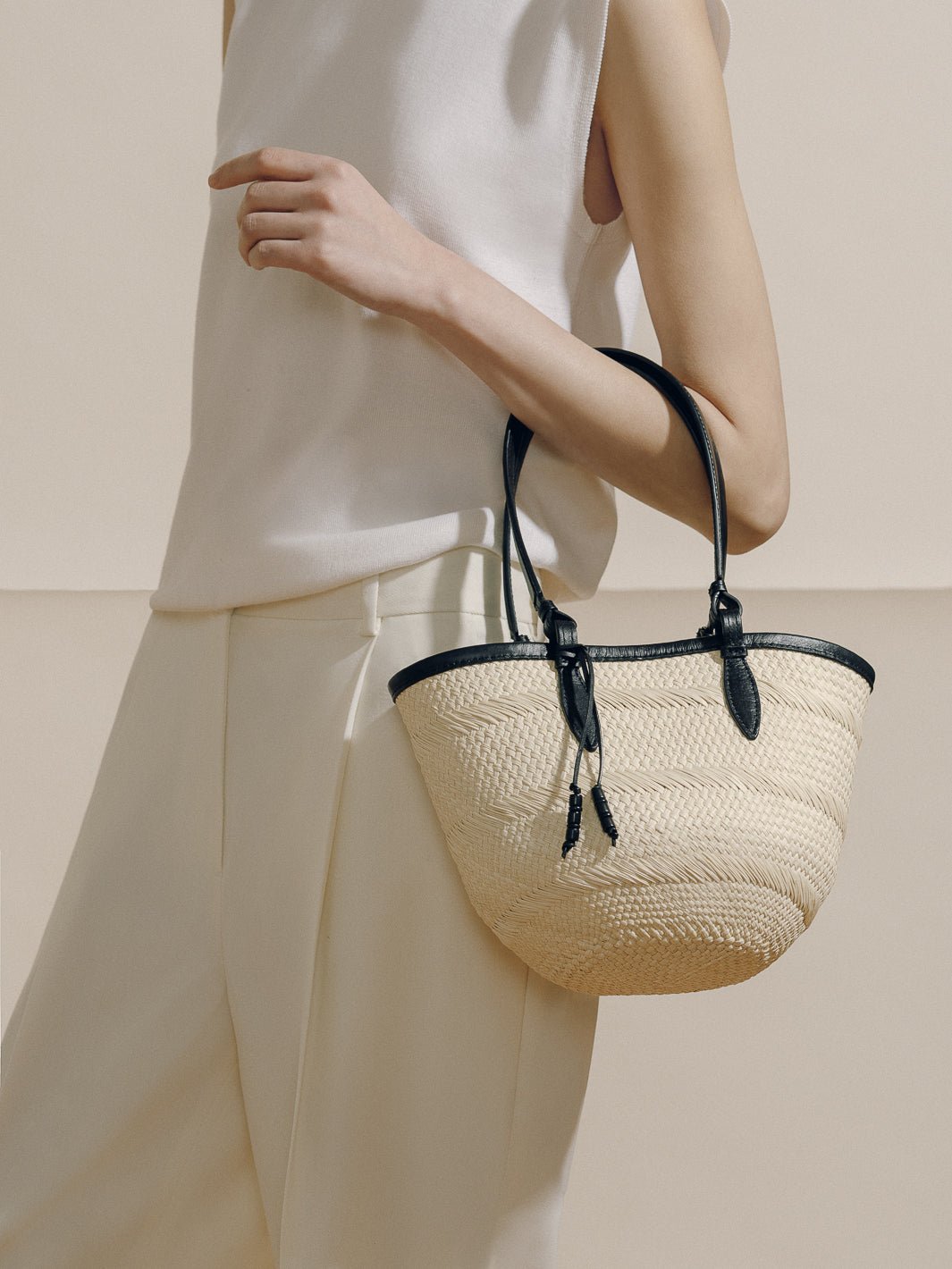 Side view of The Small Basket held by model showing woven iraca straw body with black leather trim and handles