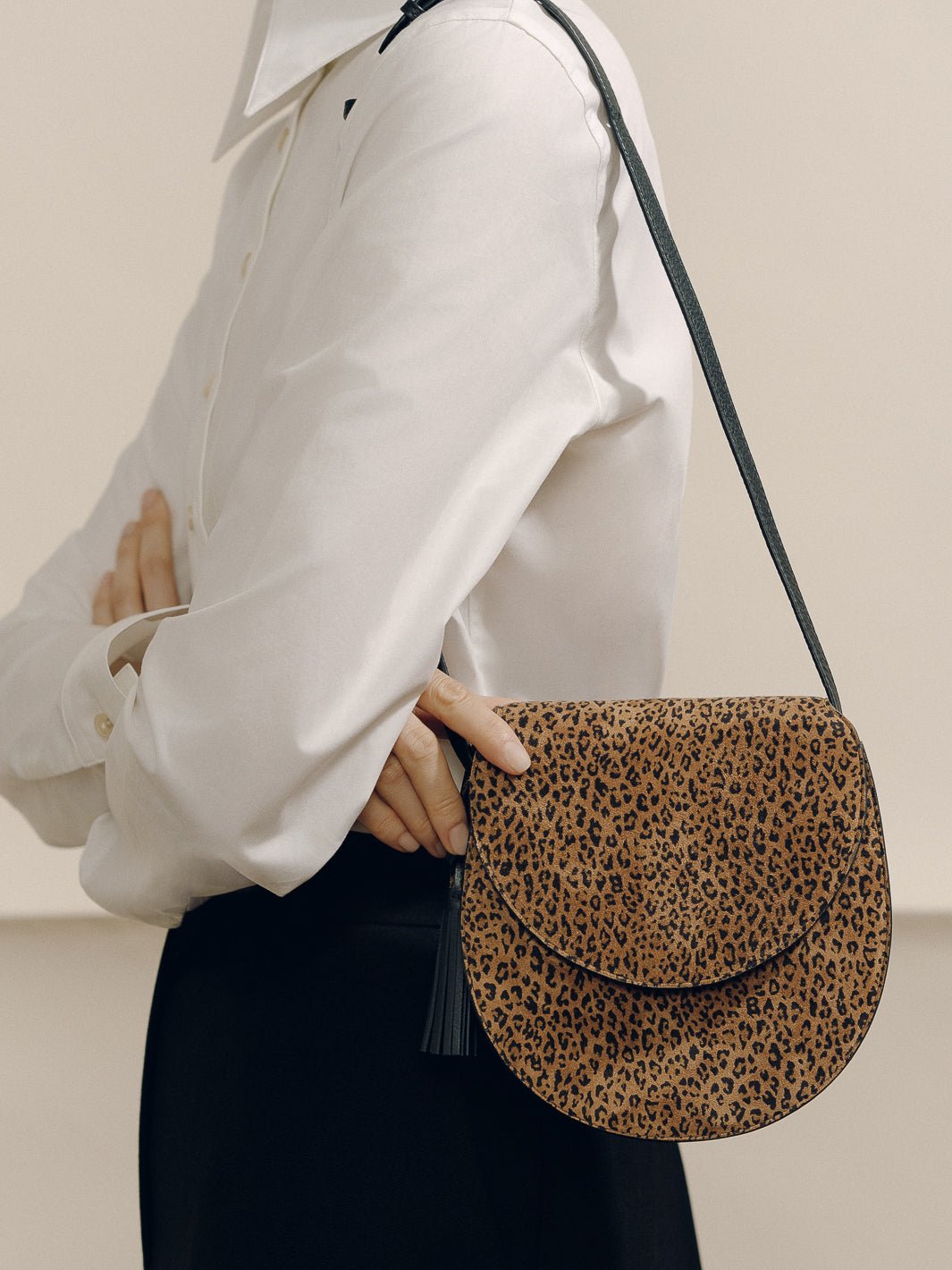 Side view of The Small Saddle Bag in Animal Print Suede showcasing leopard-print suede and removable leather tassel on a model